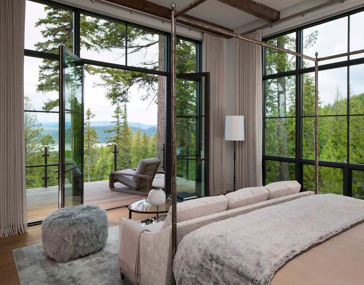 a bedroom with large windows and a bed in front of the glass wall that overlooks trees