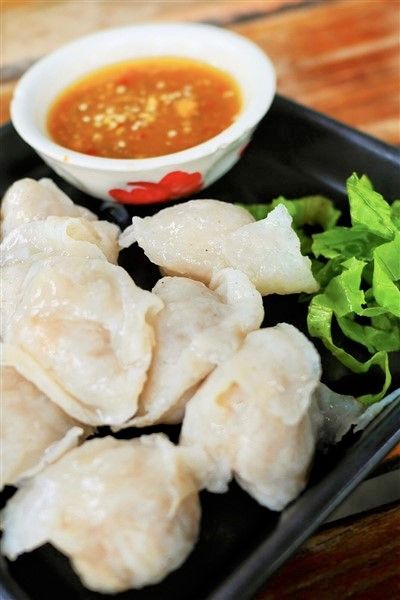 a black tray topped with dumplings and lettuce next to a bowl of dipping sauce