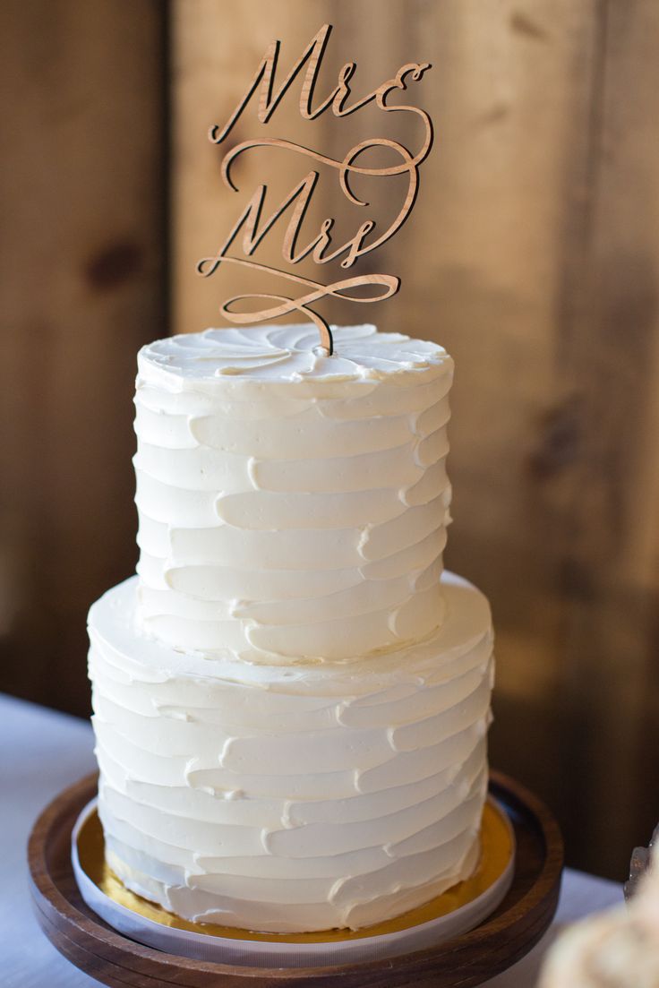 a white wedding cake with a mr and mrs topper on it's stand