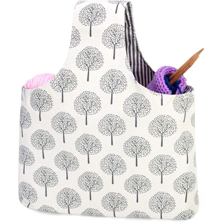 a white bag with trees on it and a crochet hook in the pocket