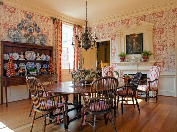 a dining room table with chairs and plates on the wall behind it, in front of a fireplace