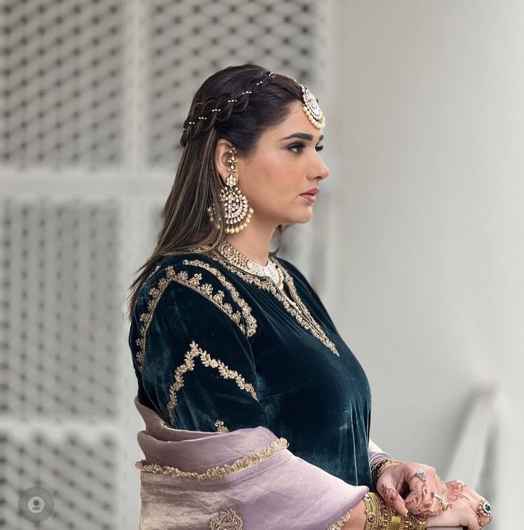 a woman in a green and purple dress with gold jewelry on her head, looking off to the side