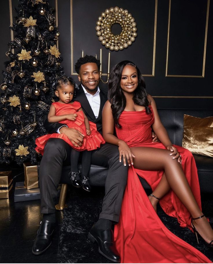 a man and woman sitting on a couch with a baby in front of a christmas tree