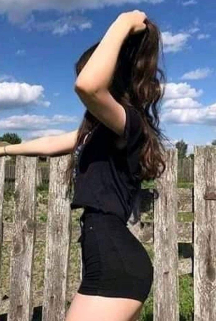 a woman in short shorts standing next to a wooden fence with her hand on the back of her head