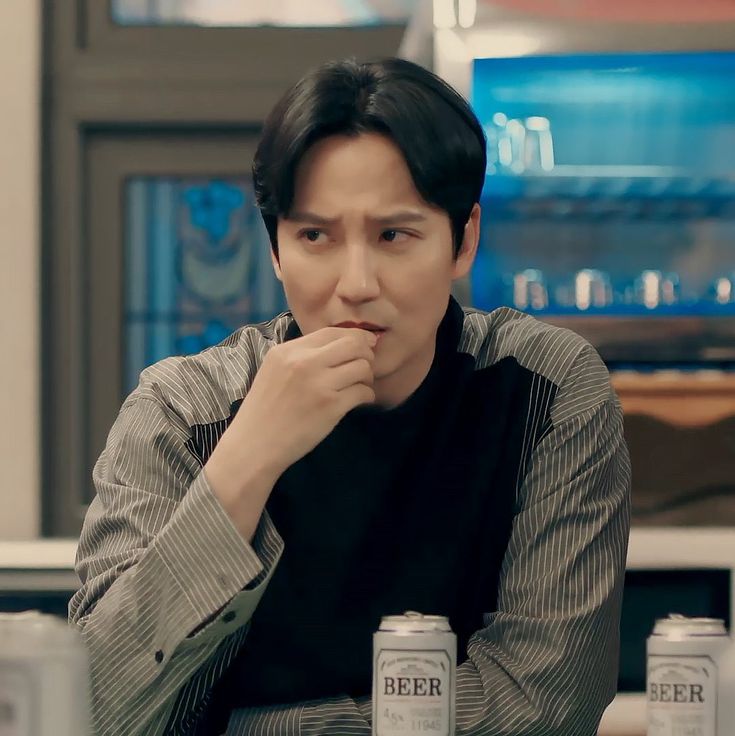 a man sitting at a table in front of three beer cans with his chin resting on his hand