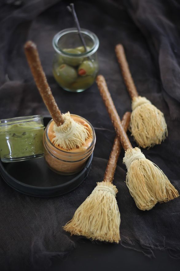 three small brooms sitting on top of a black plate next to jars with dips