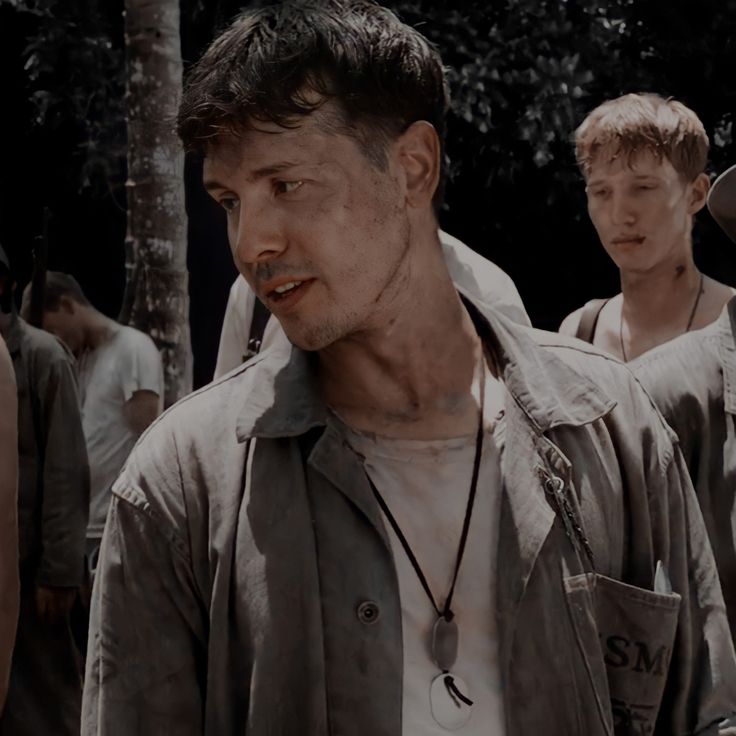 a group of men standing next to each other in front of trees and dirt on the ground