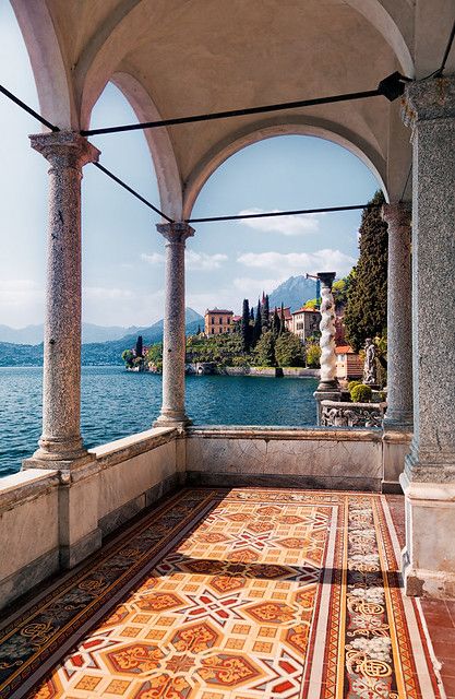 an outdoor area overlooking the water with columns and statues on it, along with mountains in the distance