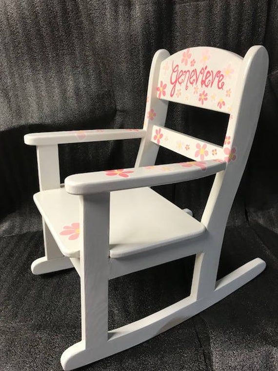 a white rocking chair with pink flowers painted on the seat and name written on it