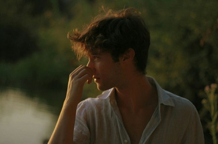 a man standing next to a body of water holding his hand up to his face