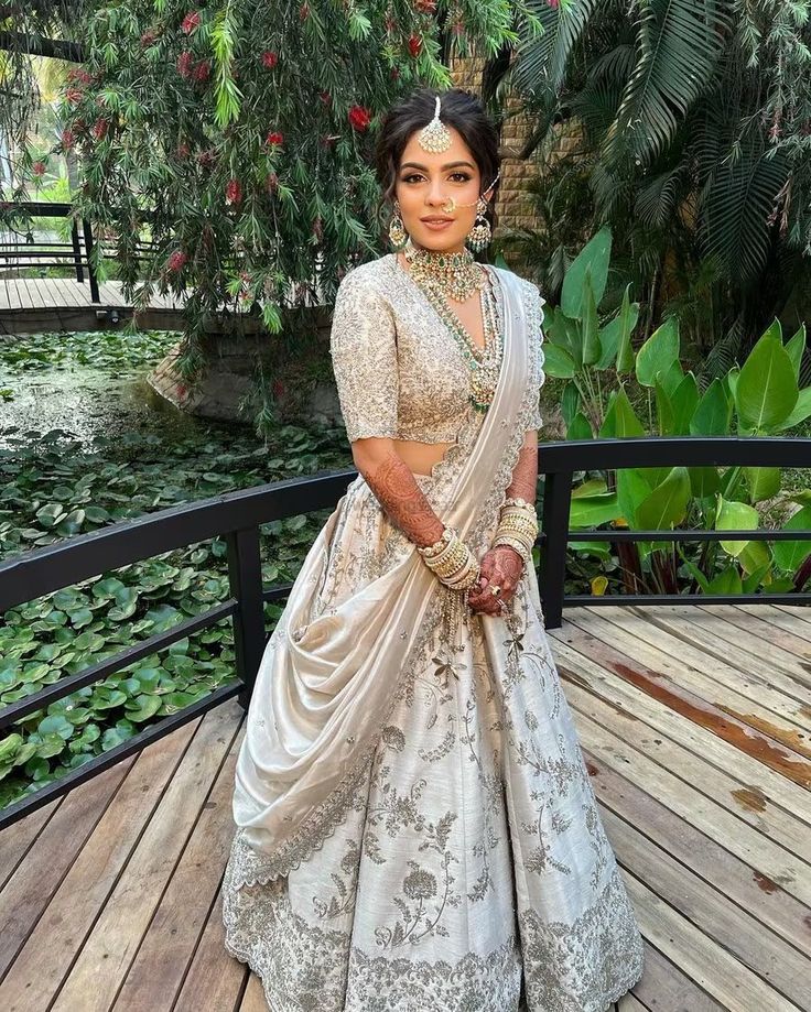 a woman in a white and gold lehenga standing on a wooden deck next to water lilies