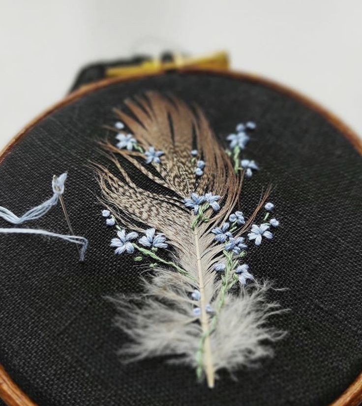 a close up of a piece of embroidery on a black cloth with flowers and feathers