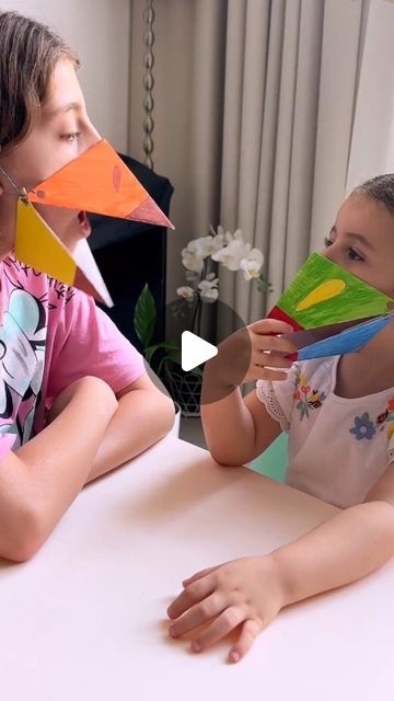 two children sitting at a table with paper airplanes in front of their faces and hands