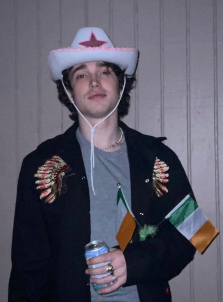 a young man wearing a hat and holding a can in his hand while standing next to a wall