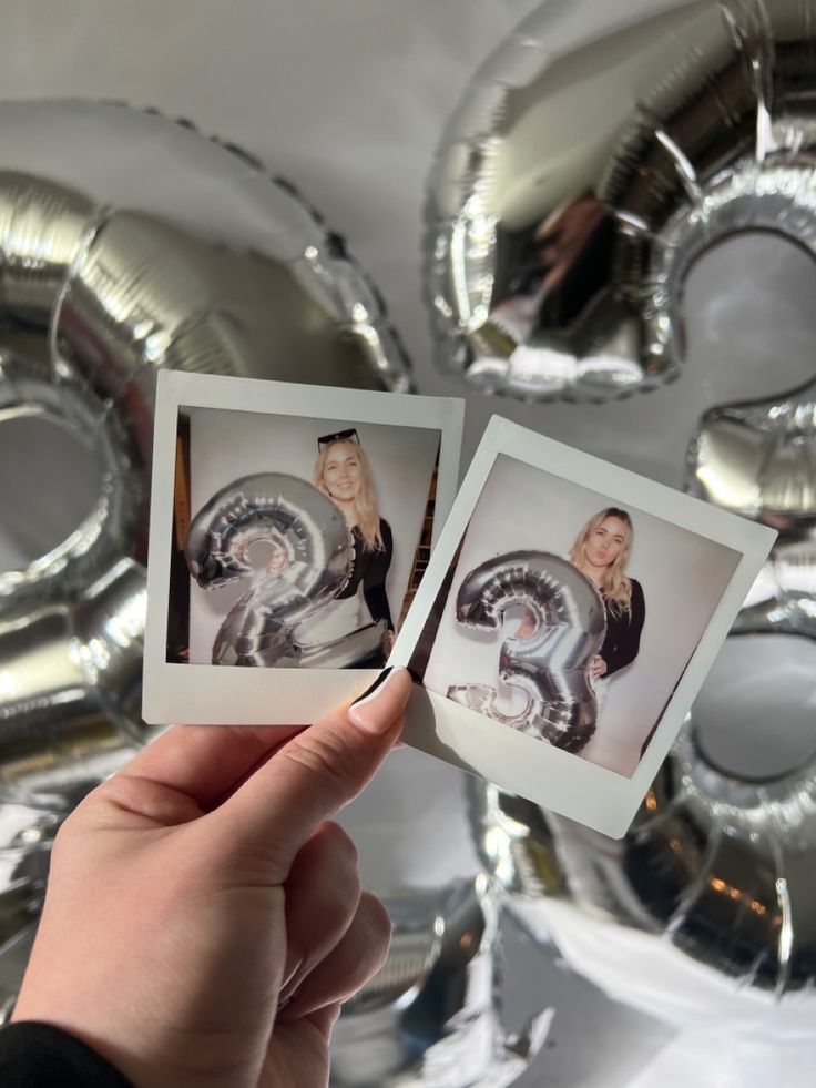 someone holding up two polaroid photos in front of some foiled balloons with the letter s on them