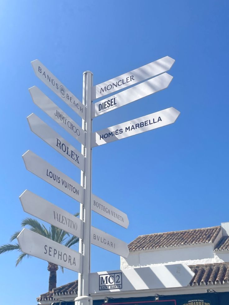 a pole with many signs on it in front of a building and palm tree behind it