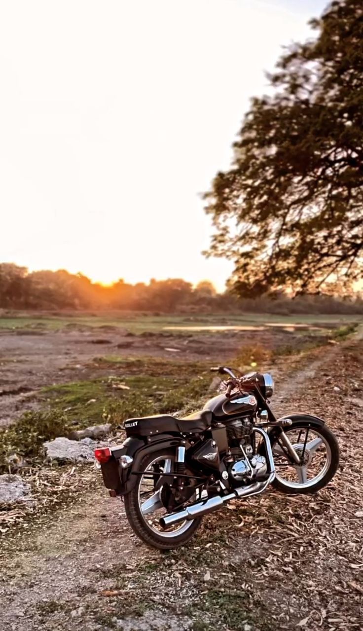 a motorcycle parked on the side of a dirt road next to a tree and grass field