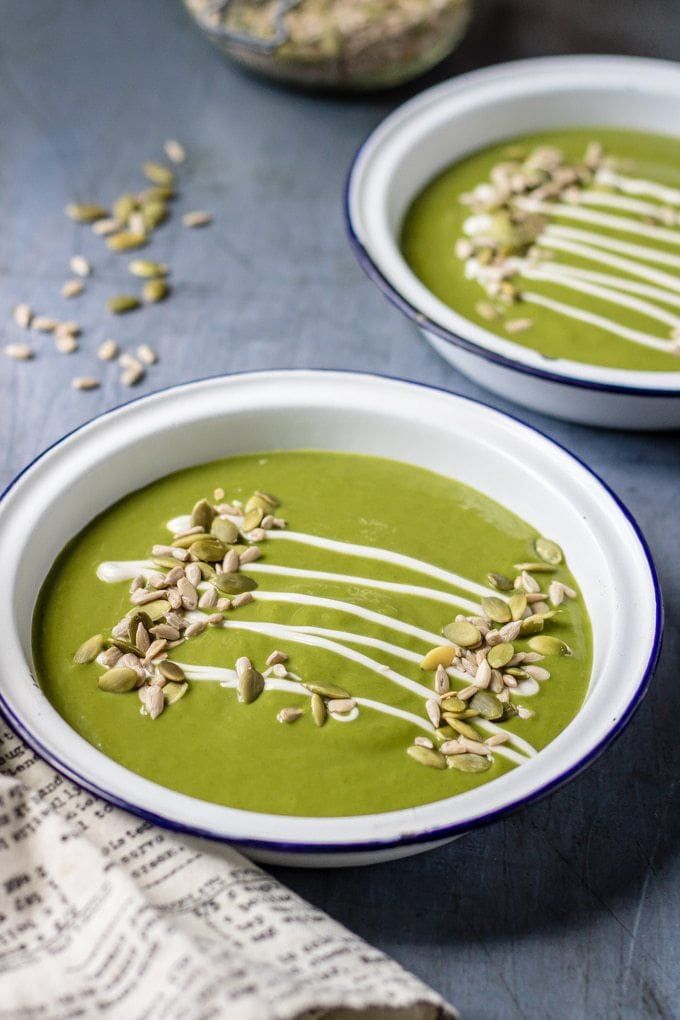 two bowls filled with green soup on top of a blue tablecloth next to some nuts