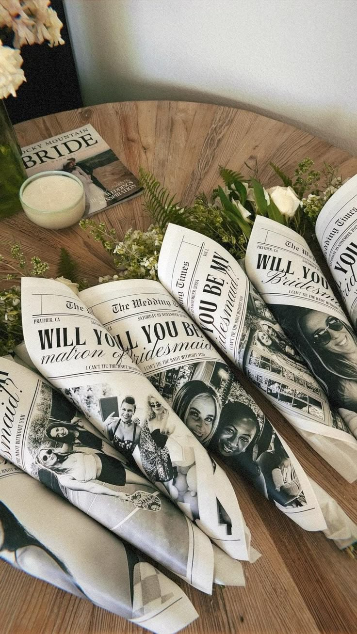 flowers and newspapers on a wooden table in front of a vase filled with white flowers