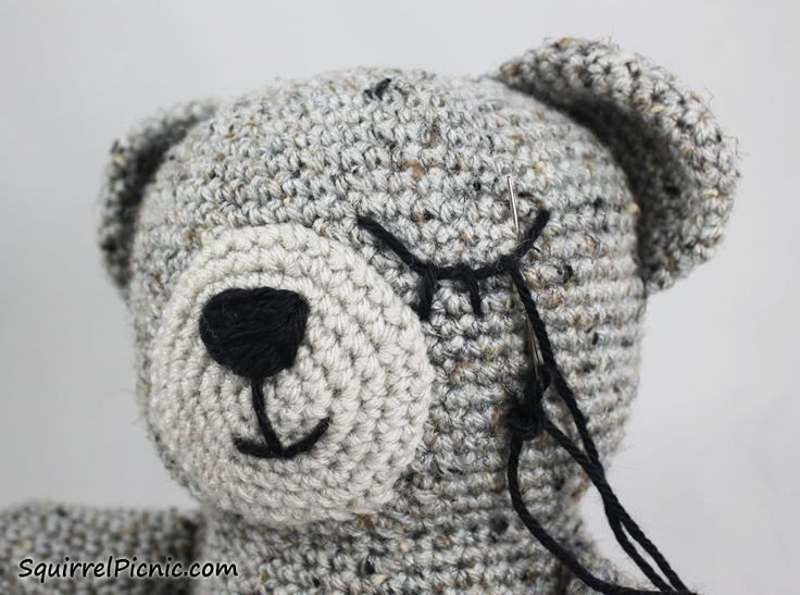 a crocheted teddy bear with a black cord on it's ear and nose