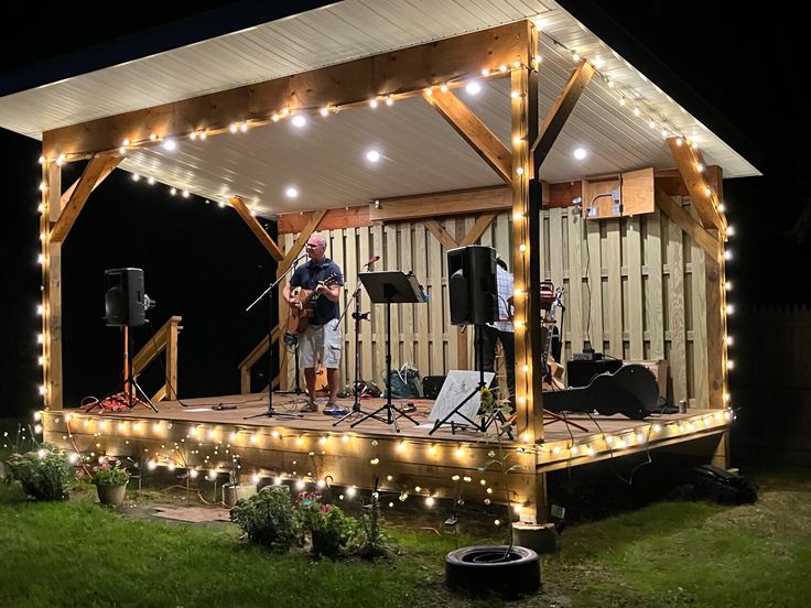 a man standing on top of a wooden deck next to a building covered in lights