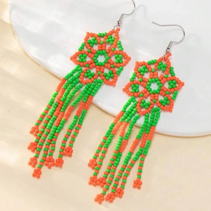 a pair of orange and green beaded earrings on top of a white plate,