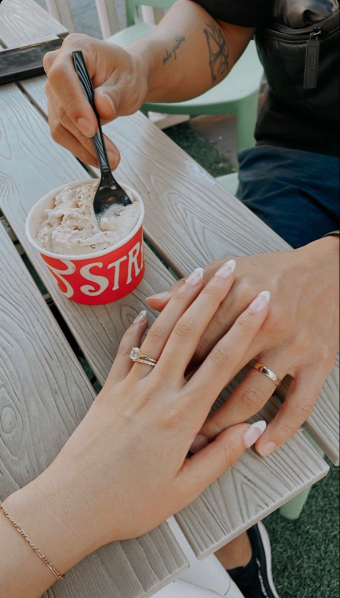 two people sitting at a picnic table with food in their hands and one holding a spoon