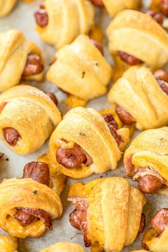 pigs in a blanket with cheese and bacon wrapped around them on a baking sheet, ready to be eaten