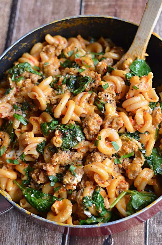 a skillet filled with pasta, meat and spinach on top of a wooden table