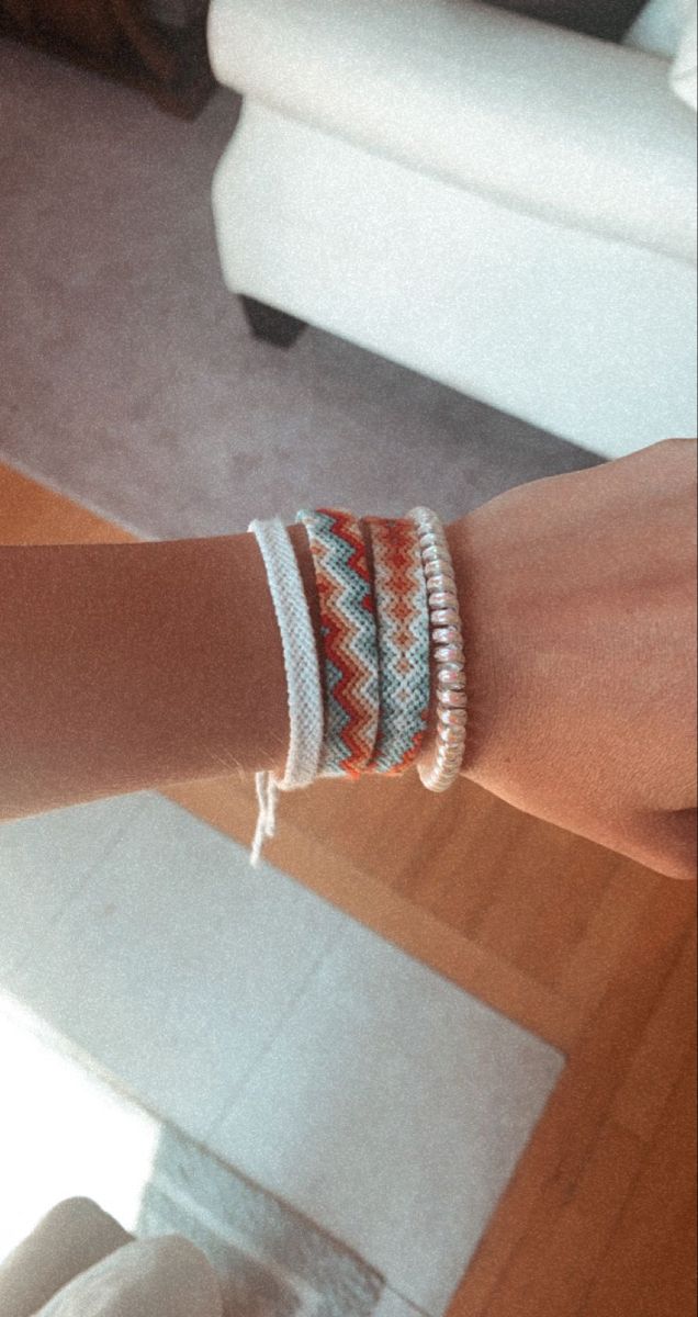 a woman's arm with two bracelets on it and a chair in the background