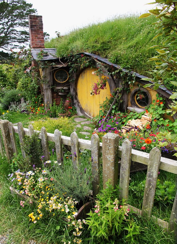 the hobbot house is surrounded by flowers and greenery, with a wooden fence