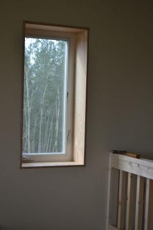 an empty room with a window and crib in the foreground, trees outside