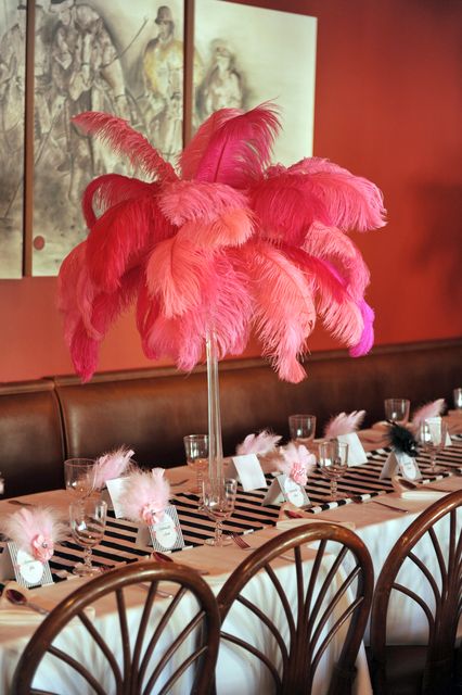 the table is set with pink feathers and place settings for guests to sit down at