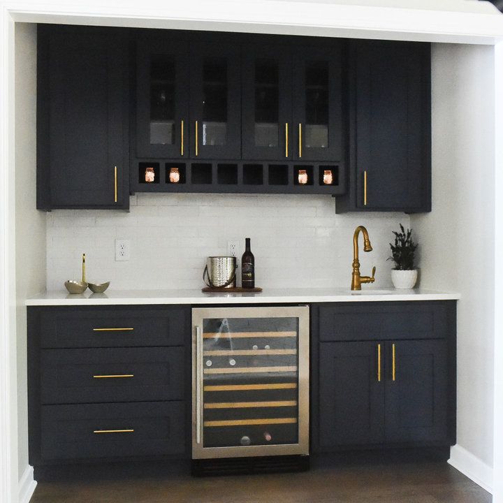 a wine cooler in the middle of a kitchen with black cabinets and gold trimmings