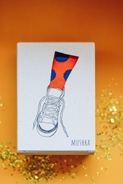 an orange sock with blue and red dots on it sitting in front of some gold glitter