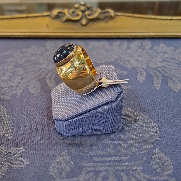 This Ring in 18k Gold with an Iolite makes a beautiful addition to any jewelry collection. The warm color of the 18k gold holds the mesmerizing Iolite for a stunning contrast. A true show stopper, this beautiful and unique ring is sure to turn heads. Timeless Gold Amethyst Ring, Formal Yellow Gold Cabochon Sapphire Ring, Yellow Gold Tanzanite Rings, Yellow Gold Tanzanite Ring With Polished Finish, Luxury Tanzanite Yellow Gold Ring, Gold Tanzanite Gemstone Rings, Luxury 14k Gold Sapphire Ring Hallmarked, Luxury 14k Gold Sapphire Ring With Hallmark, Luxury Yellow Gold Tanzanite Ring