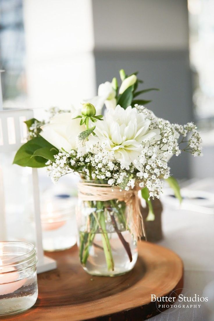 a vase filled with white flowers sitting on top of a wooden table next to a candle