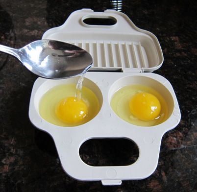 two eggs are being boiled in an egg cooker with a spoon on the side