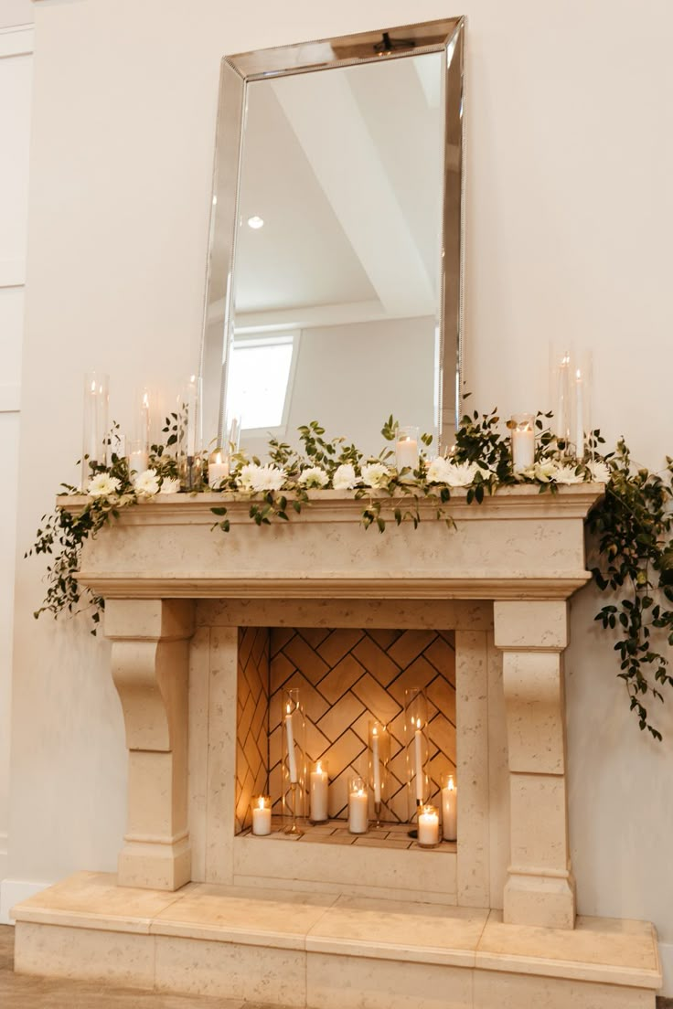 a fireplace with candles and greenery on it in front of a mirror over the mantle