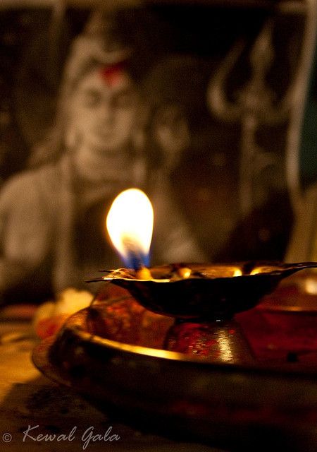 a lit candle sitting on top of a metal bowl next to a wall with pictures