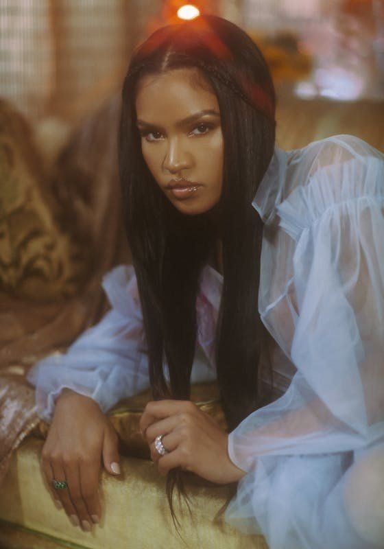 a woman with long black hair sitting on a couch wearing a white shirt and diamond ring