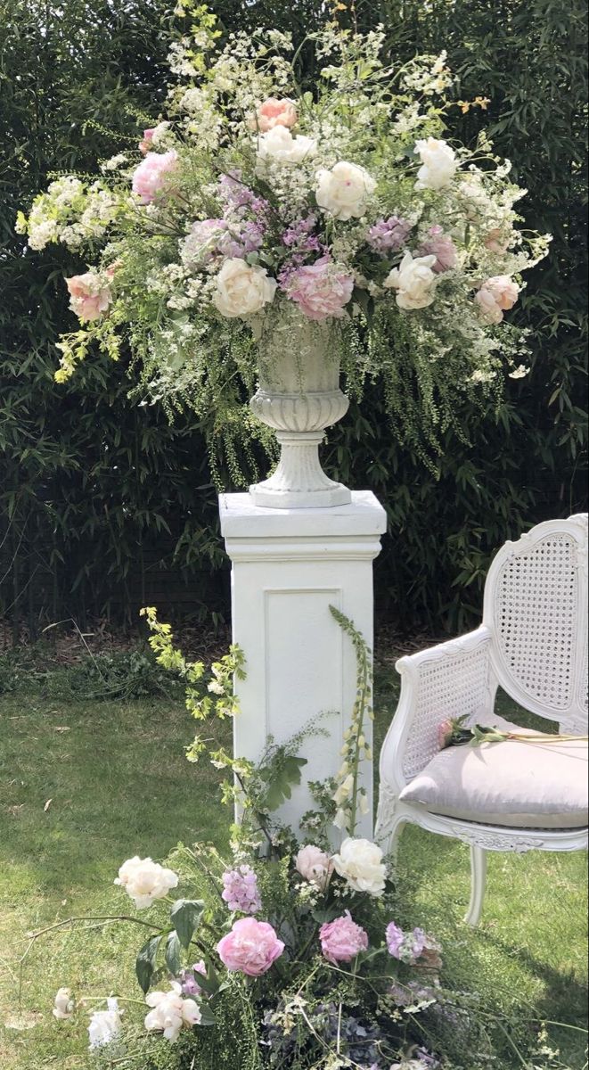 a white chair sitting next to a tall vase filled with flowers on top of a lush green field