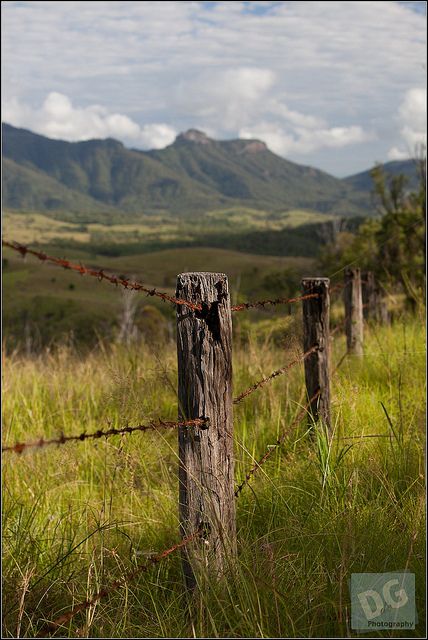 a wooden fence with barbed wire in the foreground and mountains in the distance behind it