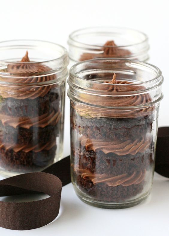 three glass jars filled with brownie desserts on top of a white table next to a black ribbon