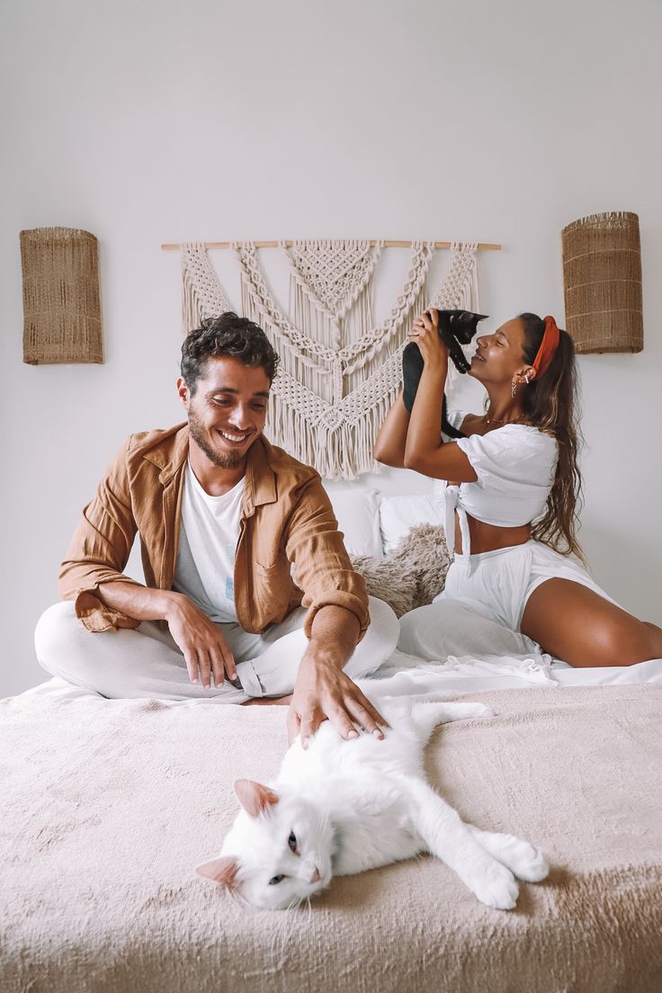 a man and woman sitting on top of a bed next to a white cat