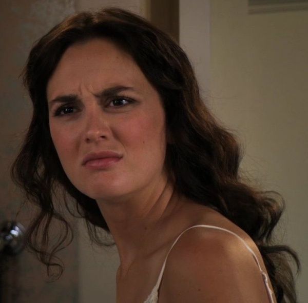 a woman in a white tank top looking at the camera while brushing her teeth with an electric toothbrush