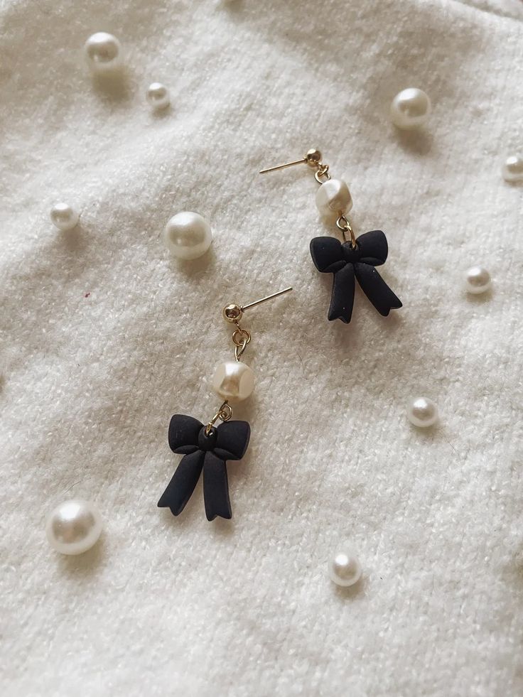 two pairs of earrings with black bows and pearls on a white cloth covered tablecloth