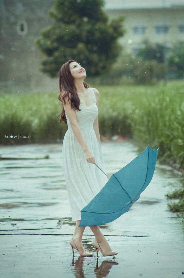 a woman in a white dress holding an umbrella and standing in the water on a rainy day