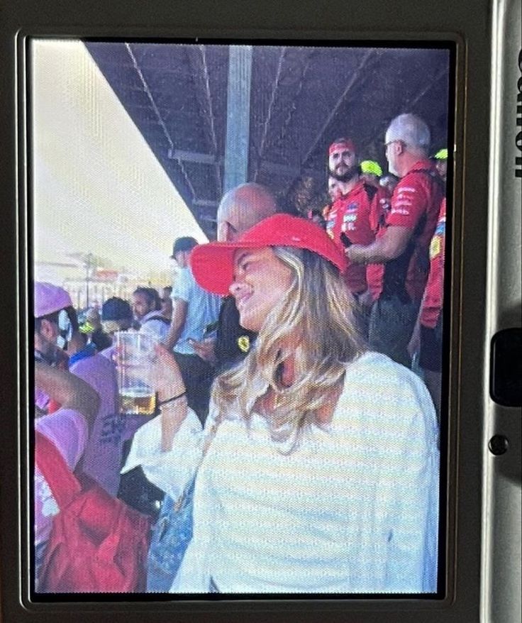 a woman wearing a red hat standing in front of a group of people at a sporting event