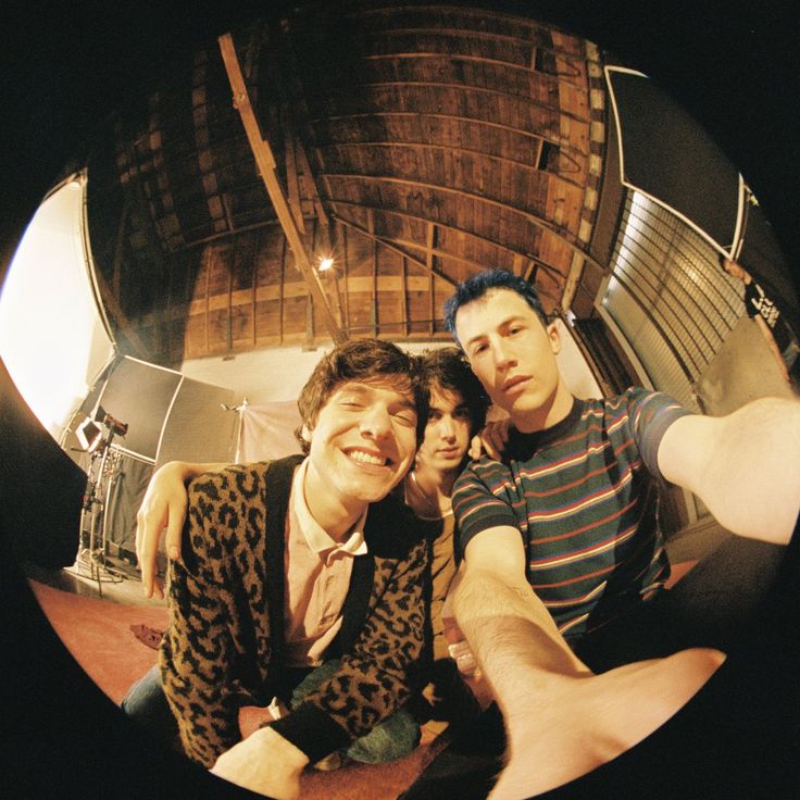 two men sitting next to each other in front of a wooden structure with metal pipes